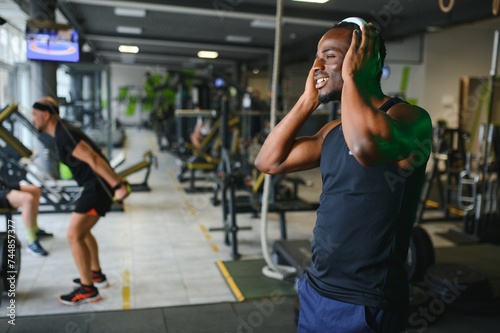 Athletic man standing in a gym listening to music using wireless headphones