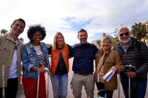 Group portrait of multiethnic happy mature people looking at the camera together enjoying their vacation with their luggage in the city street on a sunny day. © Gigi Delgado