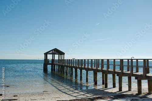 View out Bay Vista Park  with a pier on the right with leading lines of wood pier  towards Tampa Bay and the Skyway Bridge on a sunny afternoon in St. Petersburg  FL. Sunlight and reflections in water