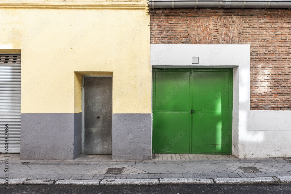 Gray access doors and a larger green one to a ground floor premises with a security lock on a cement and brick facade