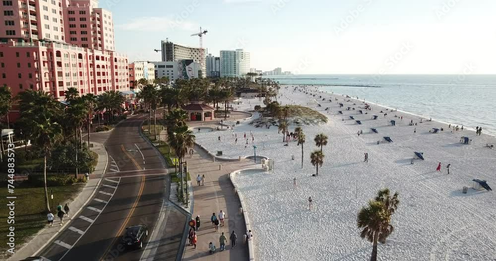 4K high resolution aerial drone video footage of a sandy beach on a sunny day with with some clouds and people, cars, buildings and palm trees in view and a beautiful pier and horizon.
