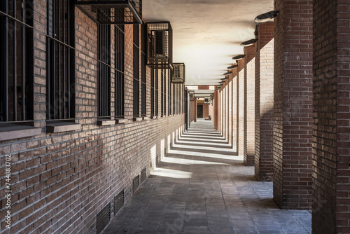 Passage on the ground floor of a brown brick building with shadows of the pillars  vanishing point and air conditioners in metal cages
