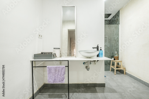 White countertop in a small bathroom with silver semicircular sink  black metal frame and a long mirror above the countertop