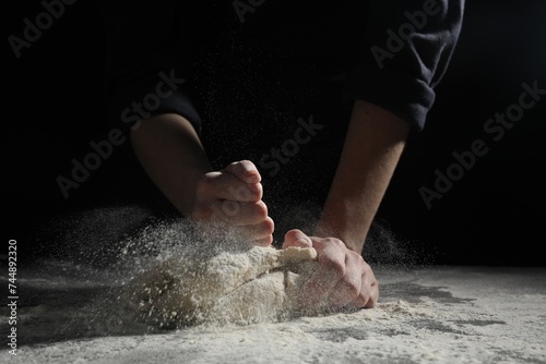 Making bread. Woman kneading dough at table on dark background  closeup