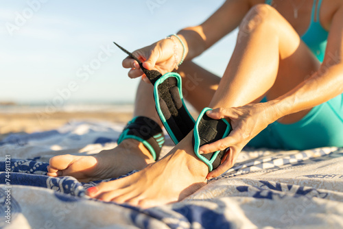 A woman puts weights, 1 kg each, on her ankles to perform Pilates exercises on the beach