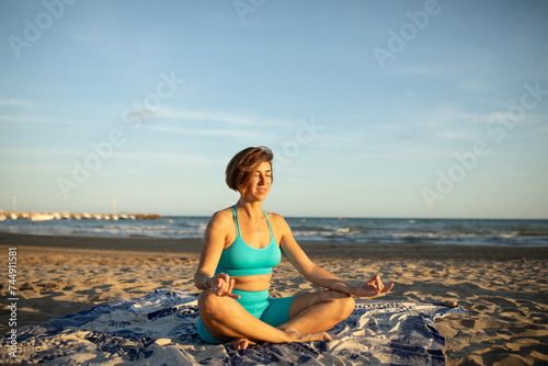 A woman performs meditation exercises on the beach, after a Pilates session at sunset