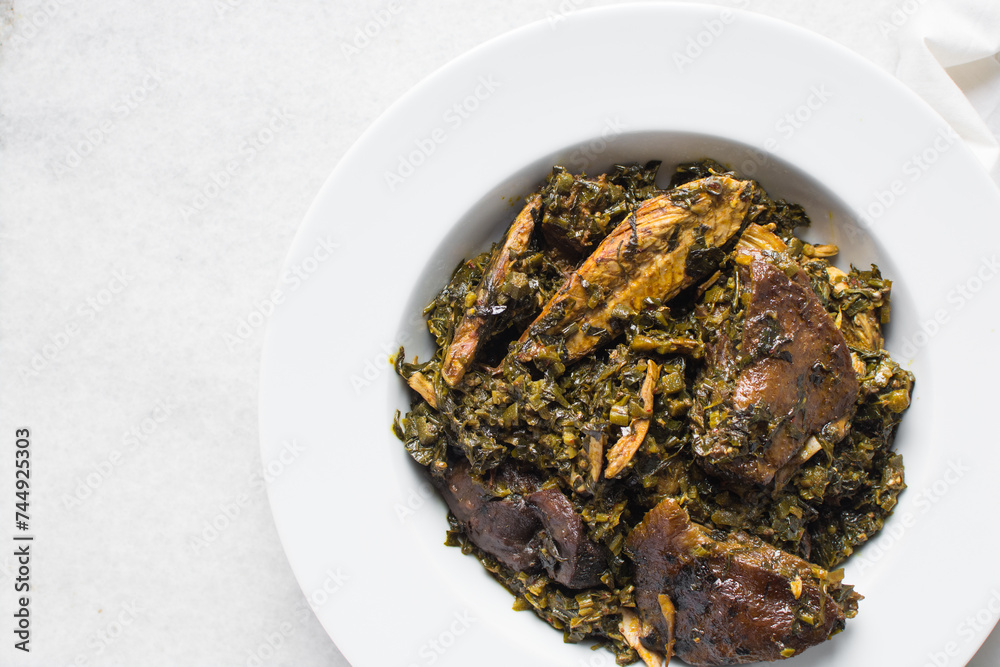 Nigerian vegetable soup with fish and bush meat in a white plate, afang soup in a large dinner plate, traditional edikang ikong soup in a white dish Nigerian vegetable soup with fish and bush meat in a white plate, afang soup in a large dinner plate, traditional edikang ikong soup in a white dish