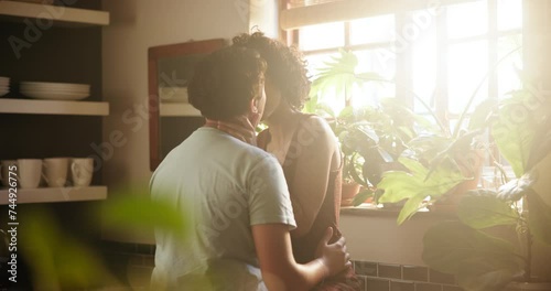 Happy woman, lesbian couple and kiss for love, embrace or intimacy by window in kitchen at home. Female person, LGBTQ or gay people with smile for romance, affection or care in support or bonding photo