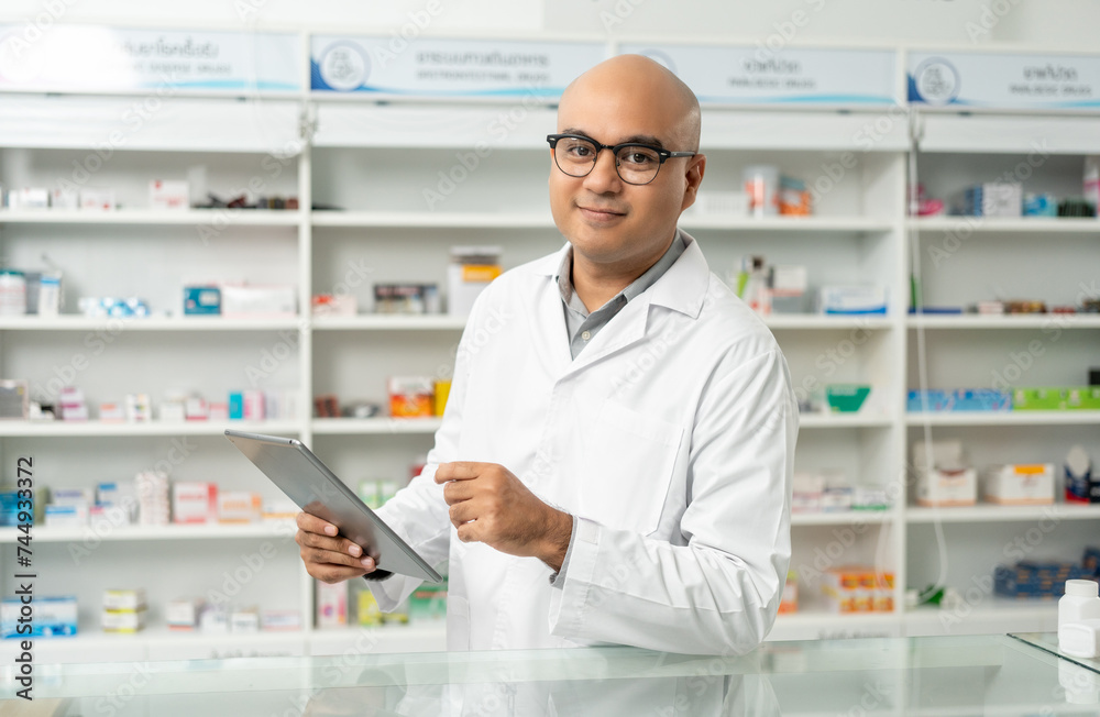 Professional asian man pharmacist checks inventory arrangement of medicine in pharmacy drugstore. Male Pharmacist wearing uniform standing near drugs shelves counter prescription to customers