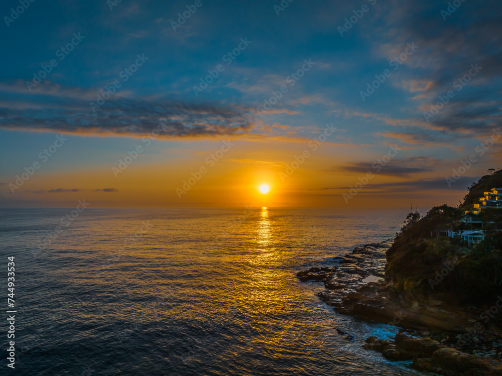 Sunrise over the calm ocean with light cloud and rocks