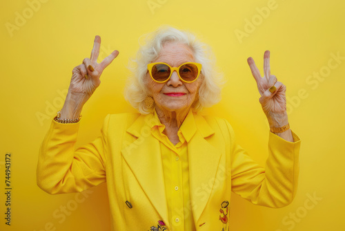 joyful senior woman in stylish blue jacket making peace sign with sunglasses