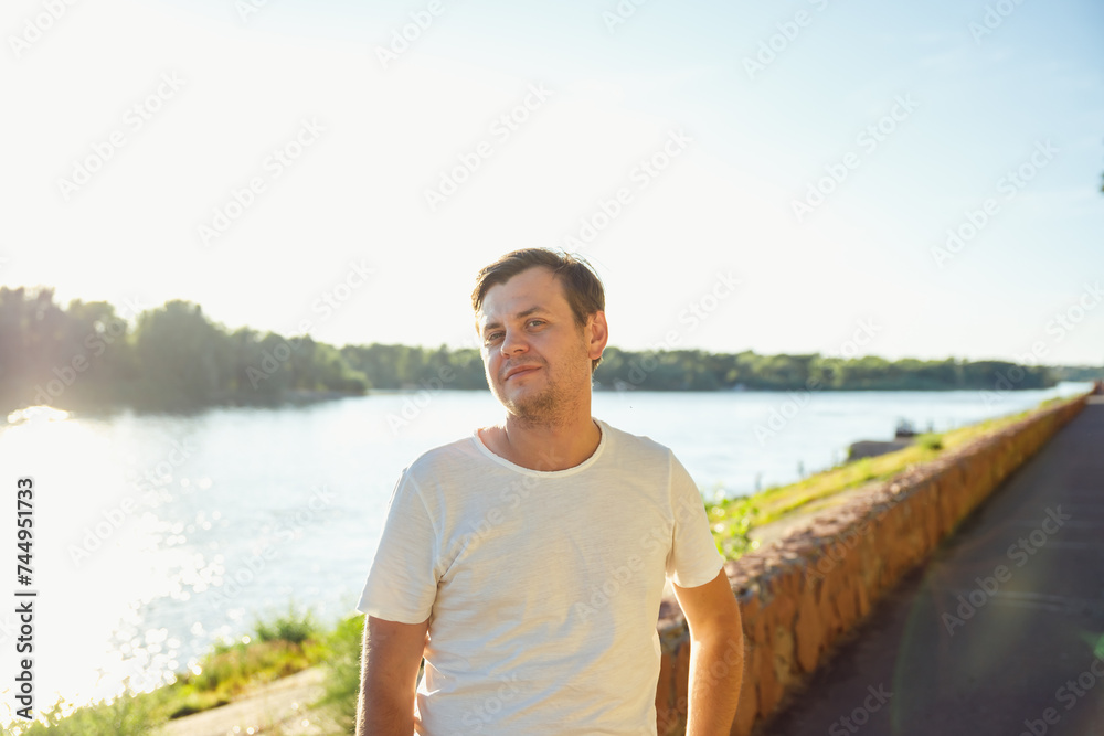 34 years old male man walks along city river embankment and rests alone in sunny day. Positive emotions, leisure activity, relax. lifestyle waist up Caucasian male portrait