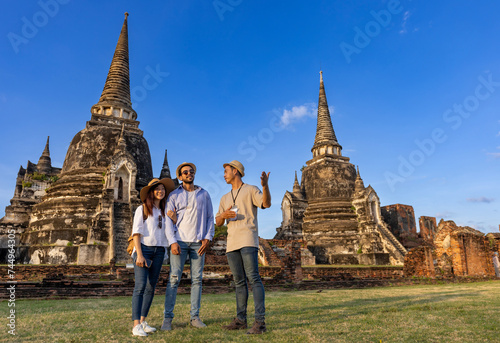Thai local tour guide is explaining the history of old Siam to the couple of tourist on their backpacker honeymoon travel to ancient temple of Ayutthaya, Thailand photo