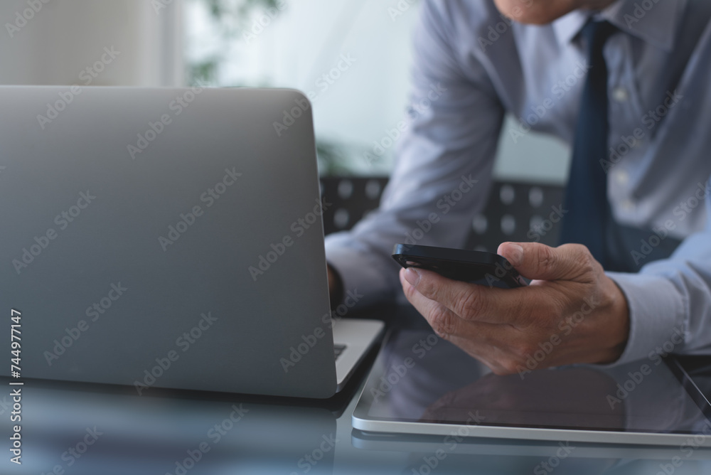Businessman using mobile phone searching the information and working on laptop computer at office. Business man online working and using smartphone surfing the internet, business concept Businessman using mobile phone searching the information and working on laptop computer at office. Business man online working and using smartphone surfing the internet, business concept