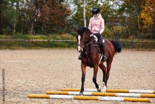 Horse with rider on the riding arena doing ground work with trotting poles. photo