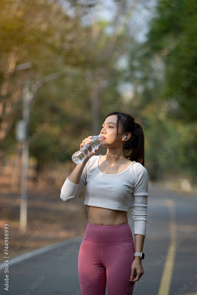 Young woman takes a break and drinks a water bottle after exercising in the park.