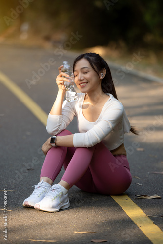 Young woman takes a break and drinks a water bottle after exercising in the park. © Wasana