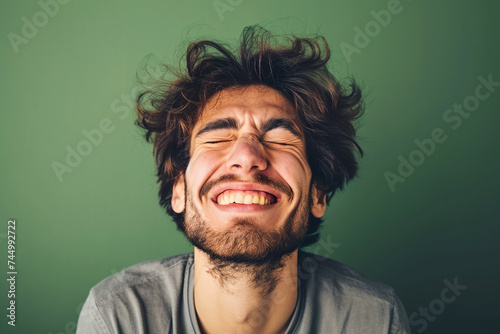 A man with his eyes closed and a twisted mouth trying to hold back laughter on a green background