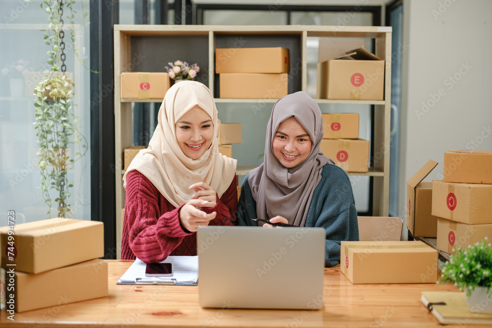 Friend muslim female two work business sme online shopping working on laptop computer with parcel box on desk at home, SME online business and delivery concept Friend muslim female two work business sme online shopping working on laptop computer with parcel box on desk at home, SME online business and delivery concept