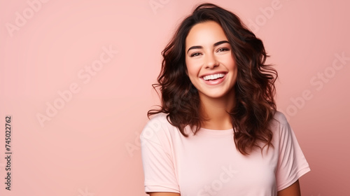 Close up of young woman with white skin, brown hair, wavy hair and a clear pink t shirt, isolated in a light pink studio. Portrait person.
