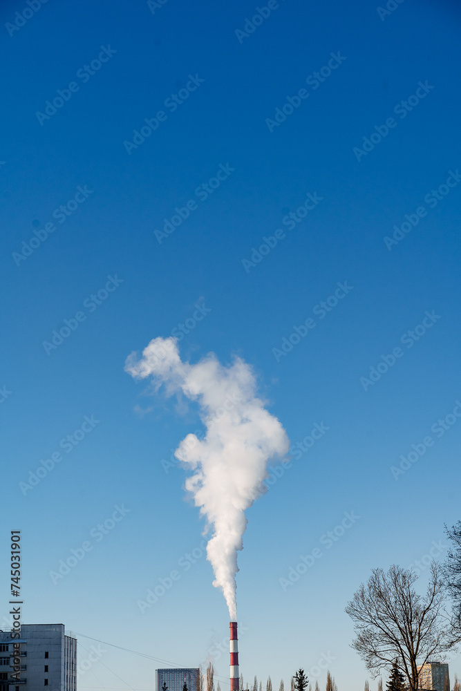 Chimney emits smoke against clear blue sky, polluting the air