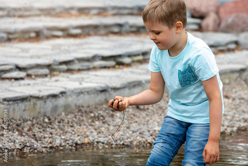 A curious boy wades in the water of a pond, a child explores the bottom by picking up wet stones