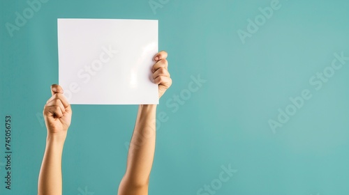 Hands holding blank sign. Concept of a person's arms raised up, presenting a white empty paper against a turquoise background, suggesting a space for text or advertisement. photo