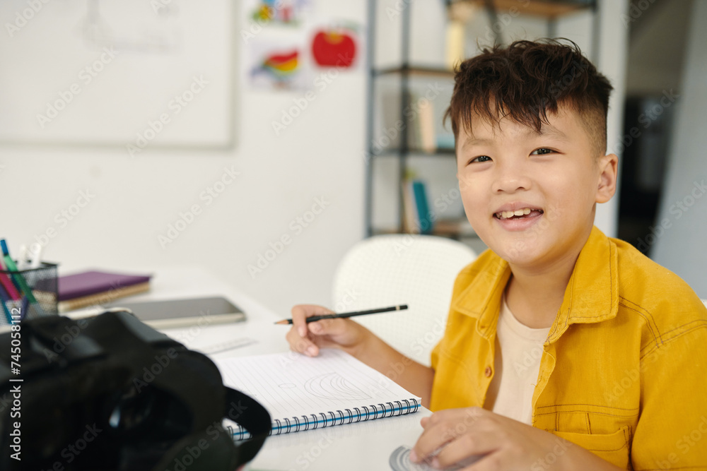 Portrait of cheerful schoolboy sitting at desk in class and writing in textbook Portrait of cheerful schoolboy sitting at desk in class and writing in textbook