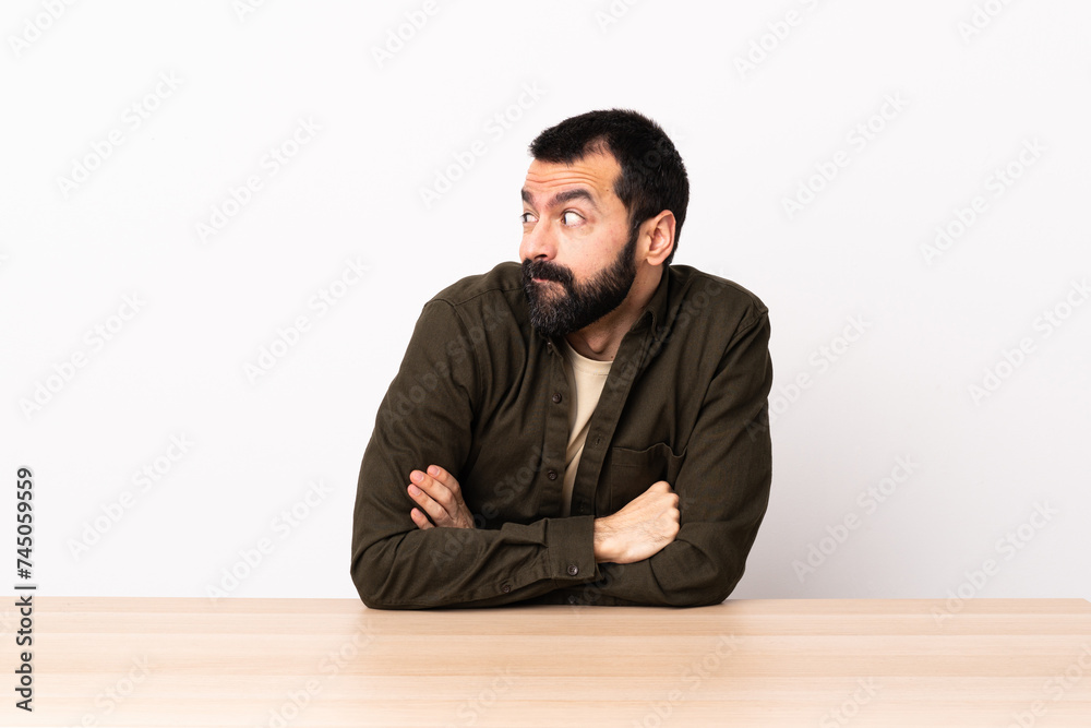 Caucasian man with beard in a table making doubts gesture looking side. Caucasian man with beard in a table making doubts gesture looking side.
