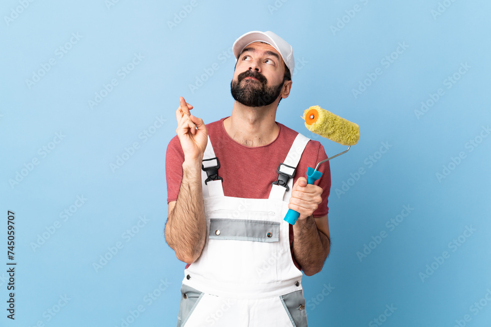 Adult painter man over isolated blue background with fingers crossing and wishing the best Adult painter man over isolated blue background with fingers crossing and wishing the best