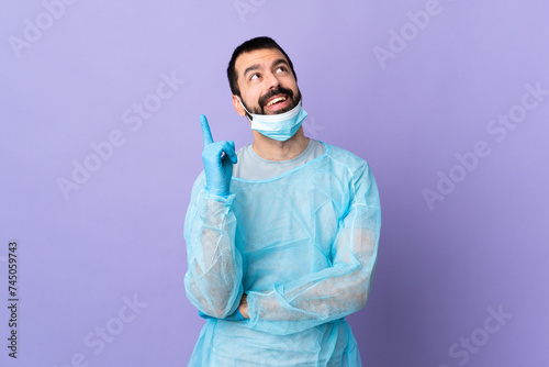 Surgeon man with beard with blue uniform over isolated purple background pointing up a great idea