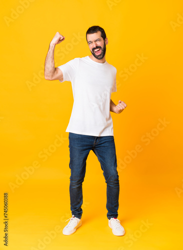 Full-length shot of man with beard over isolated yellow background celebrating a victory