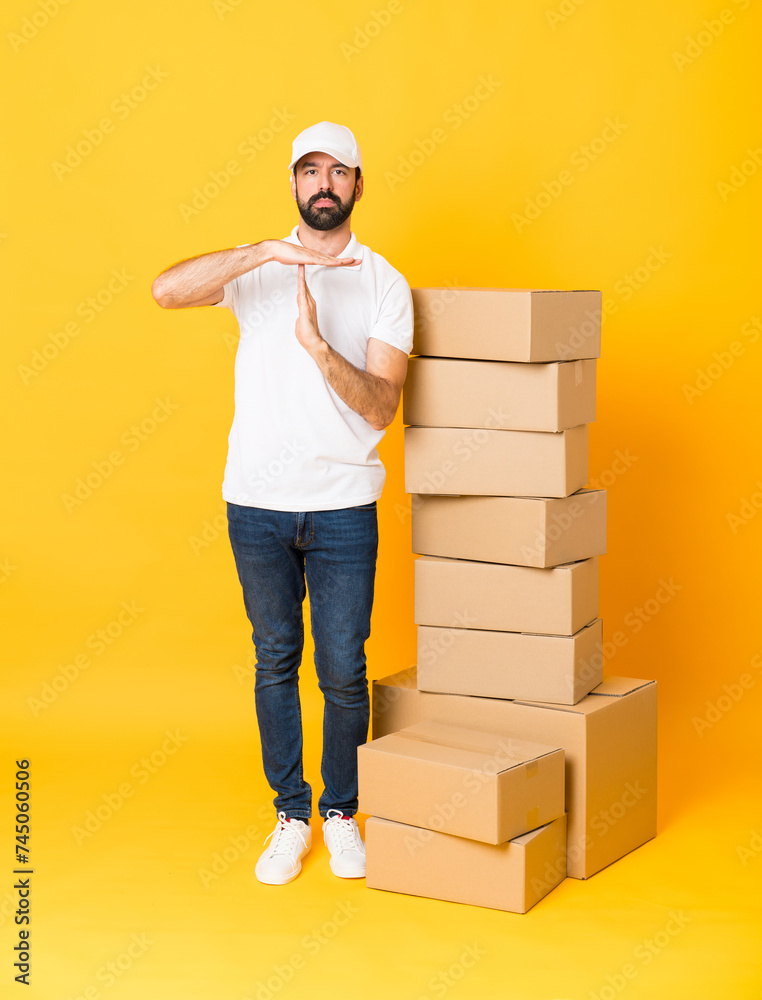 Full-length shot of delivery man among boxes over isolated yellow background making time out gesture Full-length shot of delivery man among boxes over isolated yellow background making time out gesture