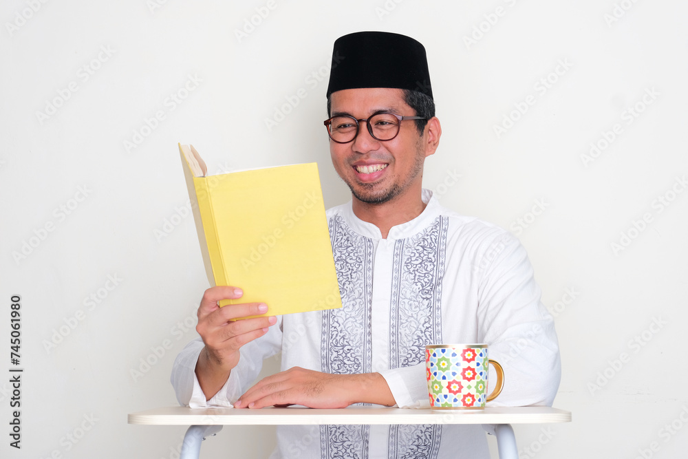 Moslem Asian man reading a book with happy expression - obrazy, fototapety, plakaty 