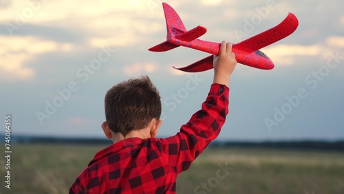 Cheerful male kid running with red airplane toy imagine pilot flight at summer field closeup back view. Adorable playful boy child flying with plane plaything fantasy imagination at evening meadow sky