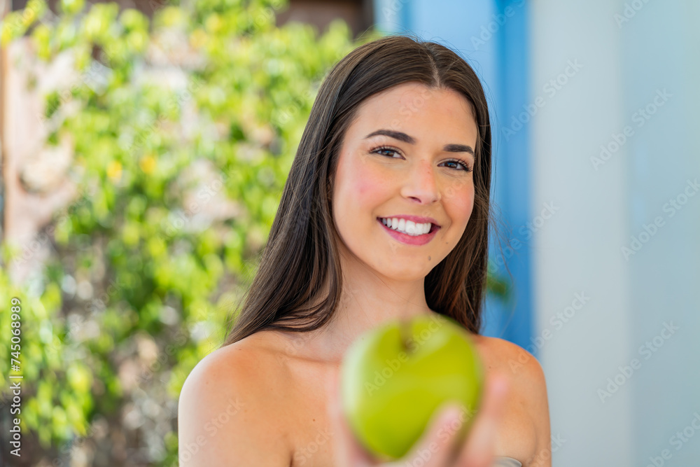 Young pretty Brazilian woman at outdoors holding an apple with happy expression Young pretty Brazilian woman at outdoors holding an apple with happy expression