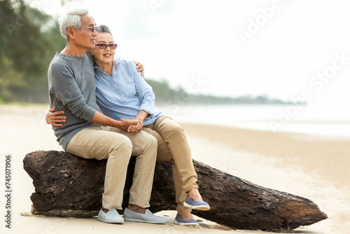 Asian Lifestyle senior couple hug and sitting on the beach happy in love romantic and relax time.  People tourism elderly family travel leisure and activity after retirement in vacations and summer