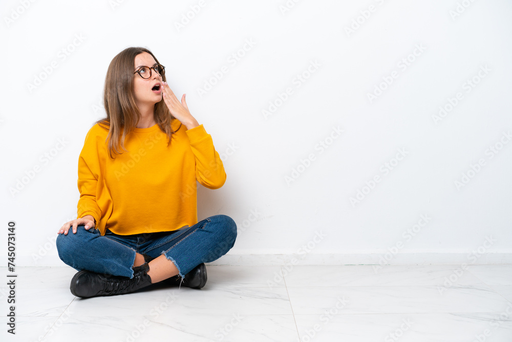 Young caucasian woman sitting on the floor isolated on white background yawning and covering wide open mouth with hand Young caucasian woman sitting on the floor isolated on white background yawning and covering wide open mouth with hand