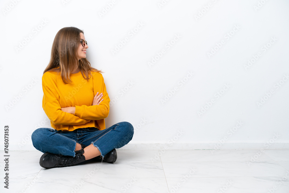 Young caucasian woman sitting on the floor isolated on white background in lateral position Young caucasian woman sitting on the floor isolated on white background in lateral position