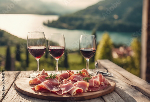 Italian appetizer prosciutto antipasti and and wine on a wooden terrace overlooking mountain lake