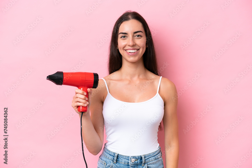Young caucasian woman holding a hairdryer isolated on pink background smiling a lot Young caucasian woman holding a hairdryer isolated on pink background smiling a lot