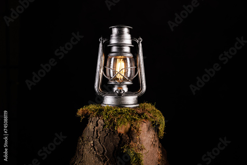 Vintage Kerosin Lampe mit LED isoliert auf einem Baumstamm mit Moos vor dunklen Hintergrund. Öllampe aus Glas. Sturmlaterne.vintage, kerosin lampe, isoliert, baumstamm, moos öllampe, sturmlaterne, cam photo