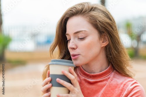 Young redhead woman at outdoors holding a take away coffee