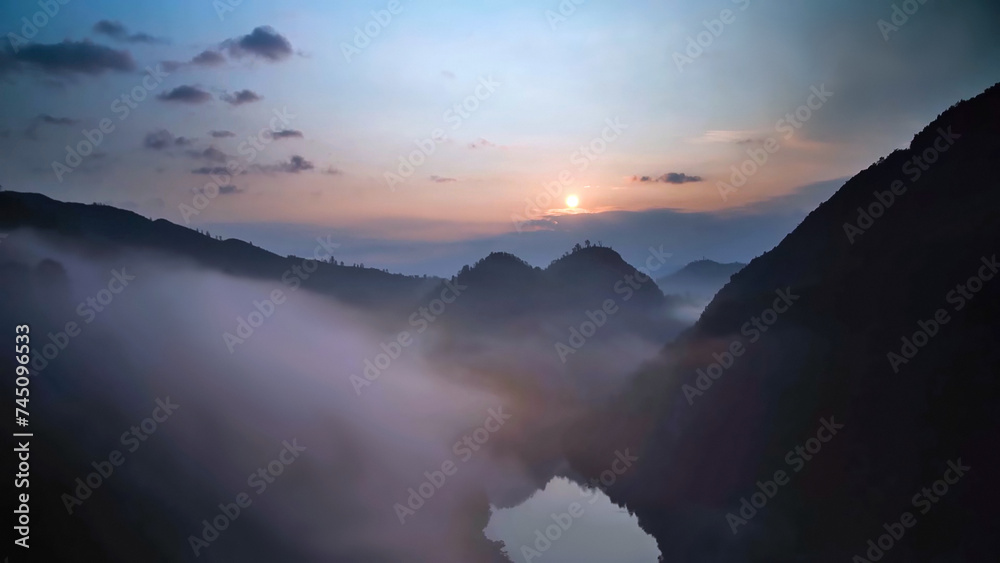 Misty view from top of mountain with a hint of sunrise. Morning sun and hilly soft dew. Cirrocumulus clouds over the river at sunrise.
