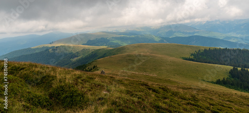 Hills of Southern Carpathians in Romania covered by mix of meadows and forests with feeding sheep photo
