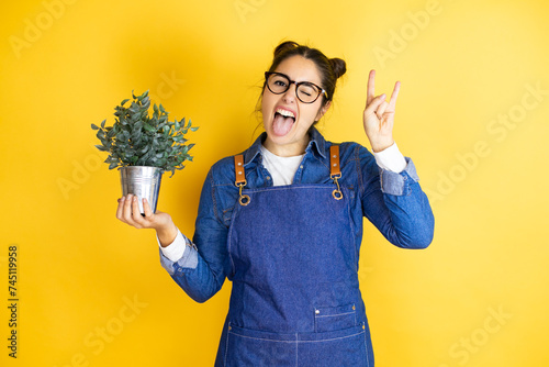 Young caucasian gardener woman holding a plant isolated on yellow background shouting with crazy expression doing rock symbol with hands up