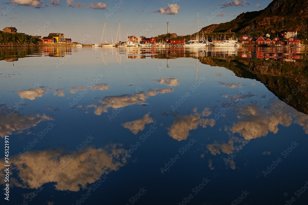 Summer houses, cabins and boats around a bay on a warm calm summer day, with clouds and their reflections in the water. Lofoten Islands, Northern Norway. 