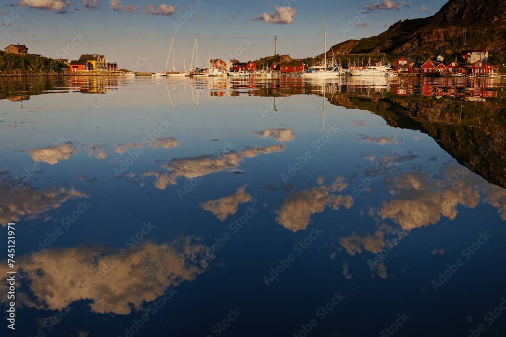 Naklejka premium Summer houses, cabins and boats around a bay on a warm calm summer day, with clouds and their reflections in the water. Lofoten Islands, Northern Norway. 