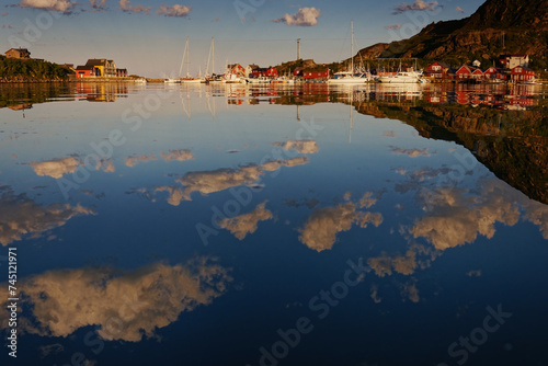 Summer houses  cabins and boats around a bay on a warm calm summer day  with clouds and their reflections in the water. Lofoten Islands  Northern Norway. 