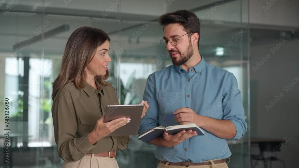 Smiling business people manager and worker working talking in office. Happy busy latin partners using digital tablet standing at work. Professional employees having conversation sharing ideas.